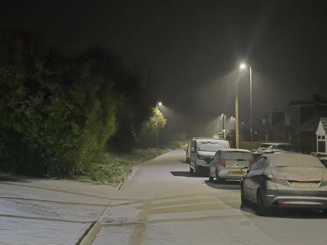 A light dusting of snow on a suburban street covers cars and road surface