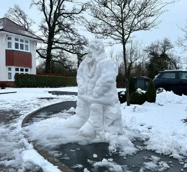 A large snow sculpture of a man on the pavement of a housing estate