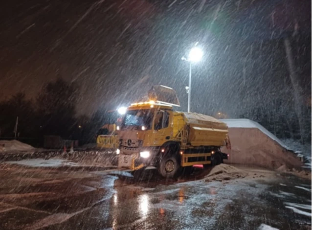 A yellow gritter with snow falling around it