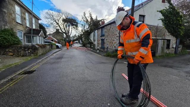 Engineers work on a road as they try to remove a tree from a house