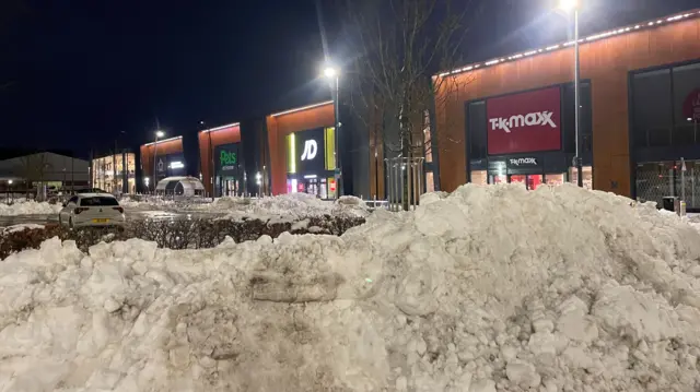 A pile of snow around bollards in front of a cleared retail park car park
