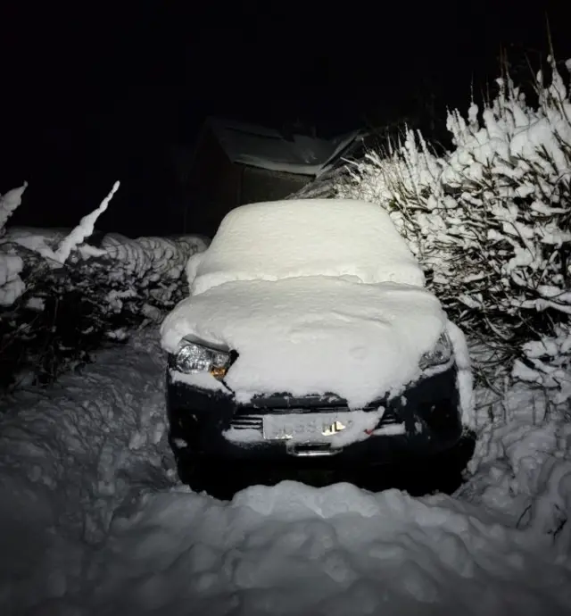 A car covered in thick snow and surrounded by it