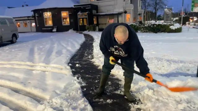 Man shovelling a path thorugh snow in front of a pub