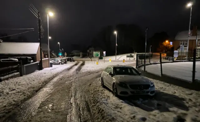 A white car is parked up in snow on the side of a snow covered road
