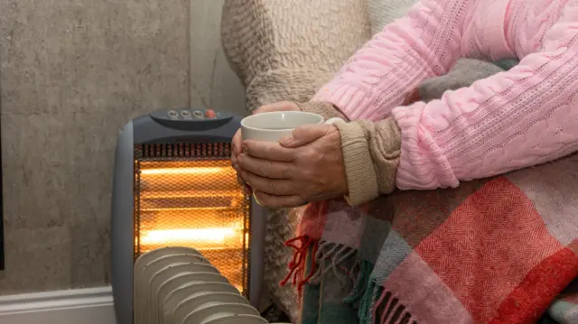Person holding a hot drink sat next to a heater
