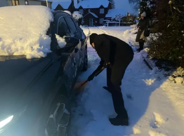 A person uses a spade to clear snow from underneath their car