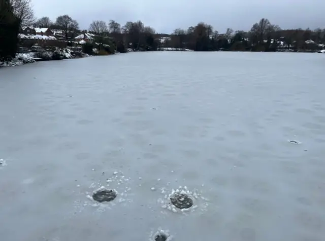 A large frozen body of water, with holes in the surface of the ice in the foreground