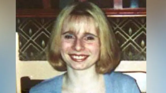 Victoria Hall smiles at the camera. She has blonde hair that is cut in a bob style. She wears a light blue top which matches blue eyeshadow she is wearing.