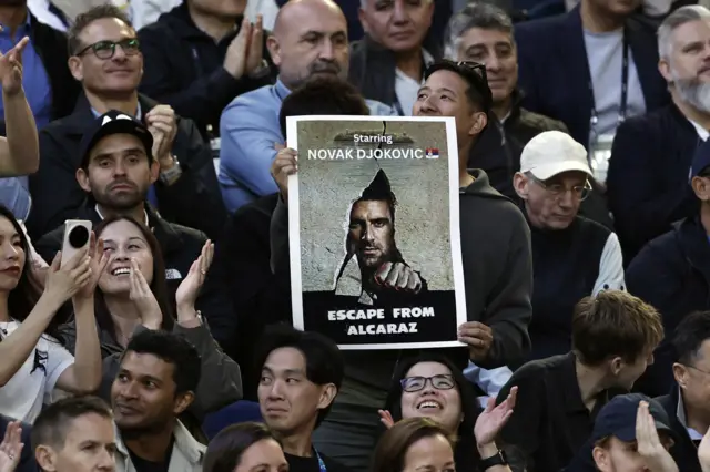 Fan in crowd holds Novak Djokovic poster