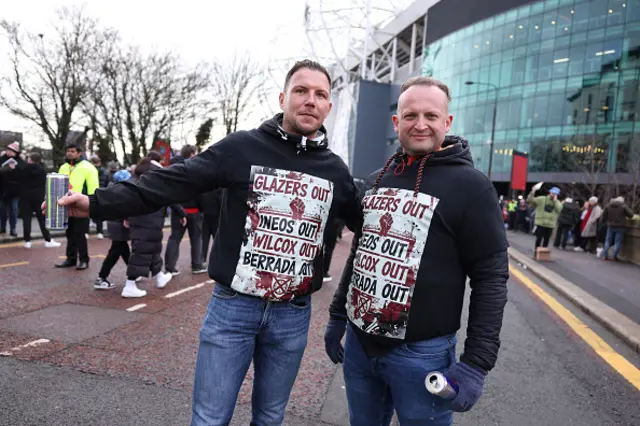 Two fans display anti-Glazer, INEOS, Wilcox and Berrada jumpers