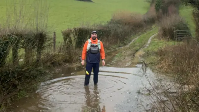 Andy Kinghan standing in a puddle on a country lane