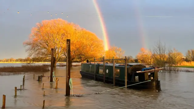 A boat sits on a flooded field with a rainbow in the sky