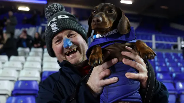 A Birmingham fans inside St Andrew's holding his support dog aloft