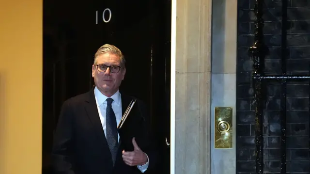 Keir Starmer in a dark suit walks out of No 10 with a black folder in his left hand