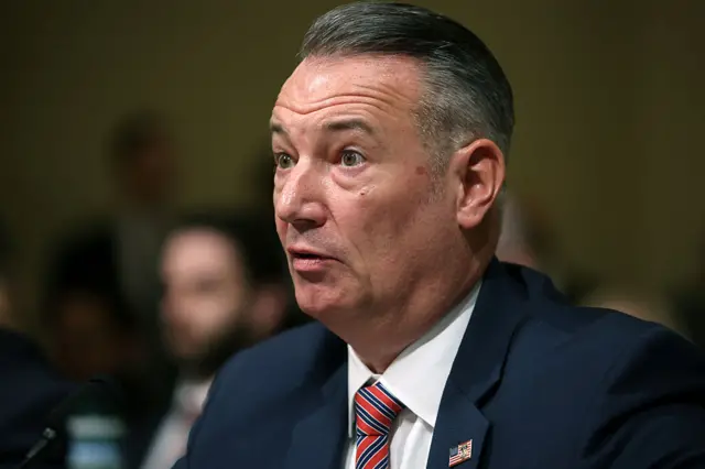 A man with greying hair, a dark blue suit and a red and blue striped tie