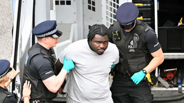 A man is held by two police officers. They are wearing bright blue gloves.