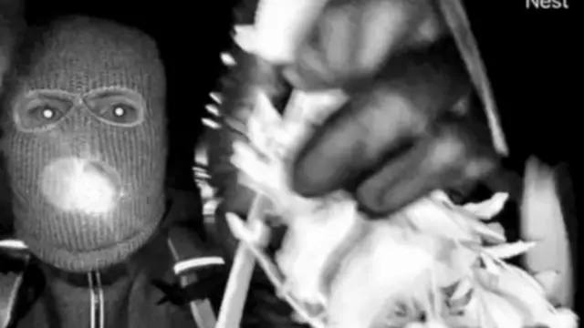 दस्ताने पहने एक नकाबपोश व्यक्ति कैमरे की ओर हाथ बढ़ाता है।