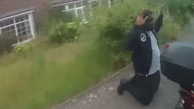 A man is on his knees with his hands in the air on the street. He is being arrested by police.