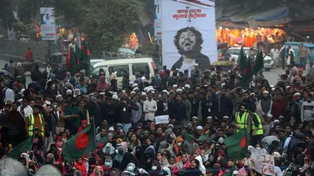A crowd gathers, with a large banner of Hadi propped up in the back.