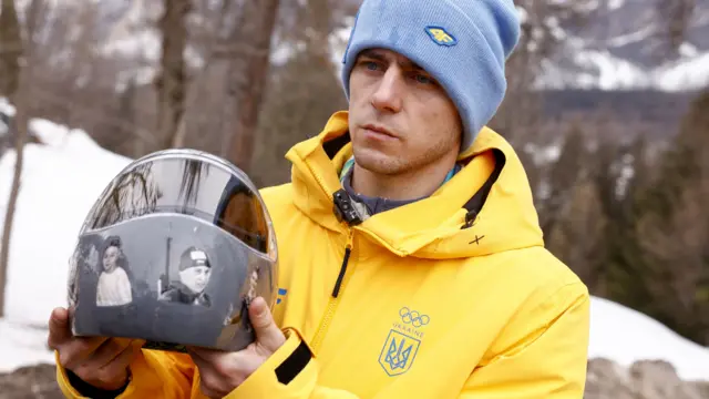 Vladyslav Heraskevych displays the helmet with images of athletes killed