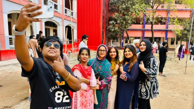 A man holds up a phone while a group of women smile behind him