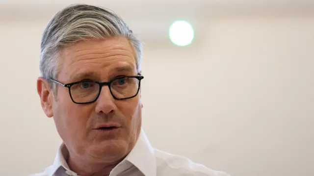 Prime Minister Keir Starmer in a white shirt against a well-lit background.