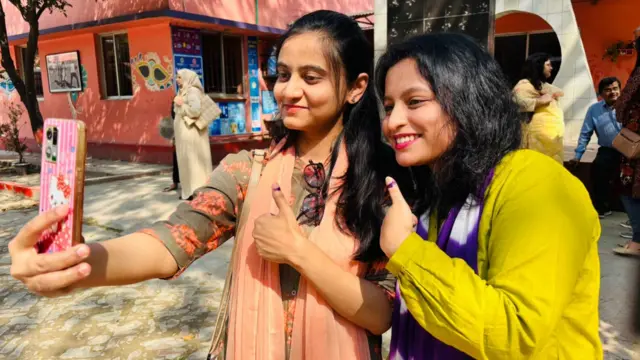 Two women pose with their thumbs up for a selfie