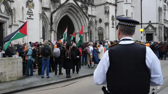 A police officer observes protesters gathered outside the High Court