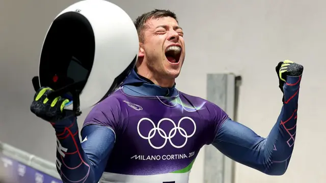 Matt Weston holds his helmet and arms aloft in celebration