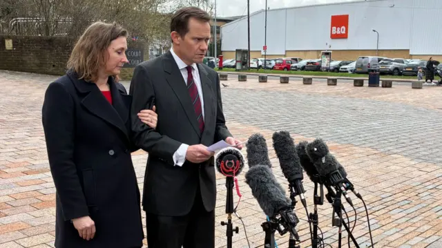 A man and woman in black stand outside a court.