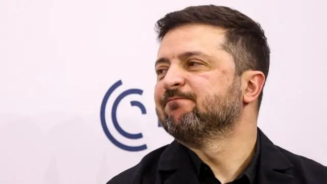 Zelensky turns to the side and smiles while on stage at the conference