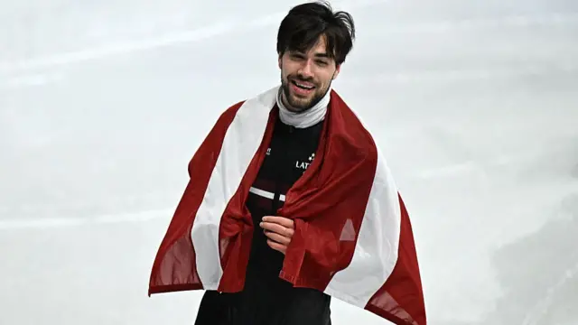 Latvia's Roberts Kruzbergs celebrates with his country's flag after winning bronze