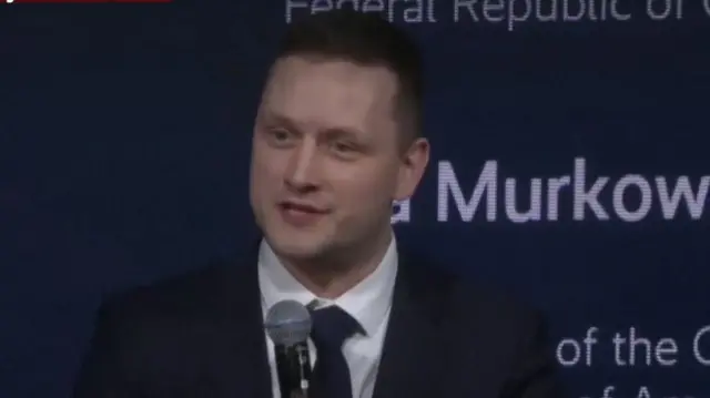 Greenland's Prime Minister Jens-Frederik Nielsen holds a microphone while speaking at a conference. He is wearing a navy suit and tie