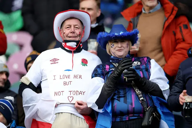 A fan of England, holding a sign which reads "I Love Her But Not Today", poses for a photograph with a Scotland fan