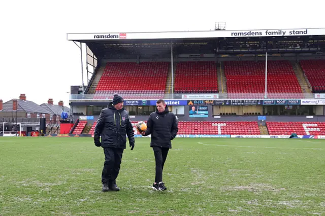 Referee, Samuel Barrott (R) and a Grimsby Town groundsman inspect the pitch