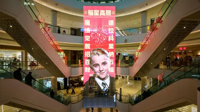 A red banner featuring a photo of Draco Malfoy hanging in the middle of a shopping mall