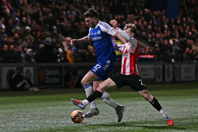 Macclesfield's English defender #12 Sam Heathcote (L) vies with Brentford's English striker #23 Keane Lewis-Potter (R) during the English FA Cup fourth round football match between Macclesfield Town and Brentford at Leasing.com Stadium, Moss Rose in Macclesfield, northern England on February 16, 2026.