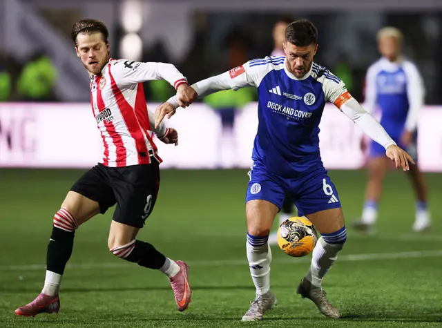 Paul Dawson of Macclesfield is challenged by Mathias Jensen of Brentford during the Emirates FA Cup Fourth Round match between Macclesfield and Brentford at Moss Rose Ground on February 16, 2026 in Macclesfield, England.
