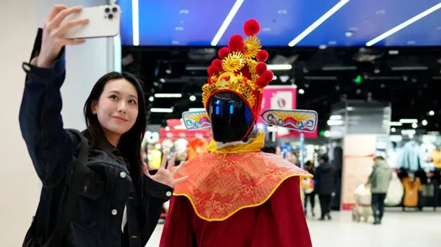 A young woman taking a selfie with a robot dressed in a red traditional Chinese costume