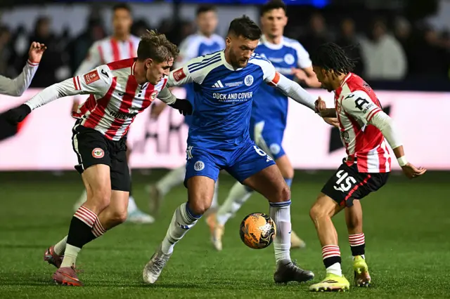 Macclesfield's English midfielder #06 Paul Dawson (C) vies with Brentford's Ukrainian midfielder #18 Yehor Yarmolyuk (L) and Brentford's English midfielder #45 Romelle Donovan (R) during the English FA Cup fourth round football match between Macclesfield Town and Brentford at Leasing.com Stadium, Moss Rose in Macclesfield, northern England on February 16, 2026.