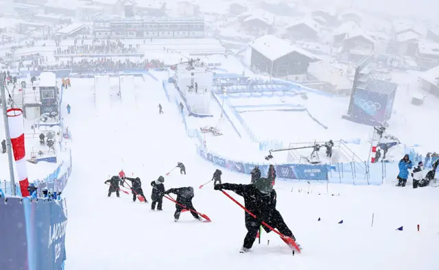 Workers clear snow as the Freestyle Skiing Women's Aerials Qualification is delayed due to adverse weather