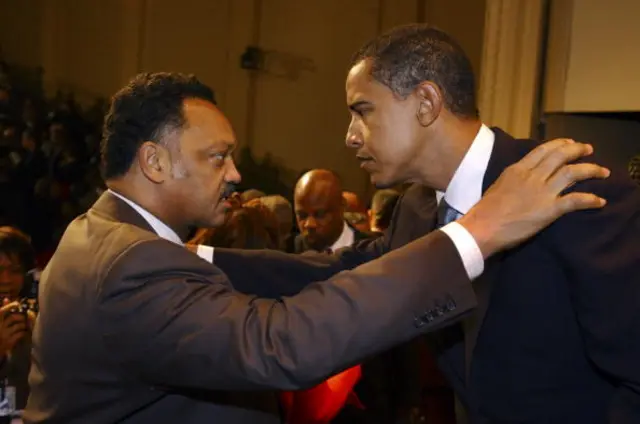 Jesse Jackson, left, puts his right arm on Barack Obama, right, as the pair face each other in a crowded room.