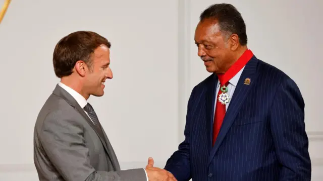 Macron and Jackson looking at each other smiling and shaking hands