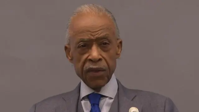 Headshot of Sharpton as he speaks in front of a grey wall
