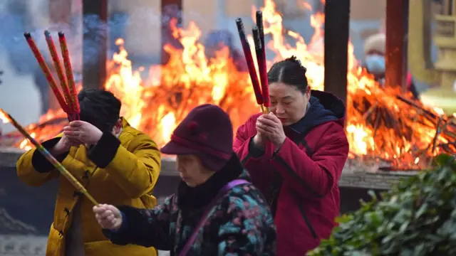People holding large incense sticks while praying with a fire burning in the background