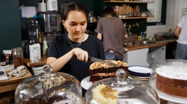 A waitress in a cafe cutting a slice of cake for a customer