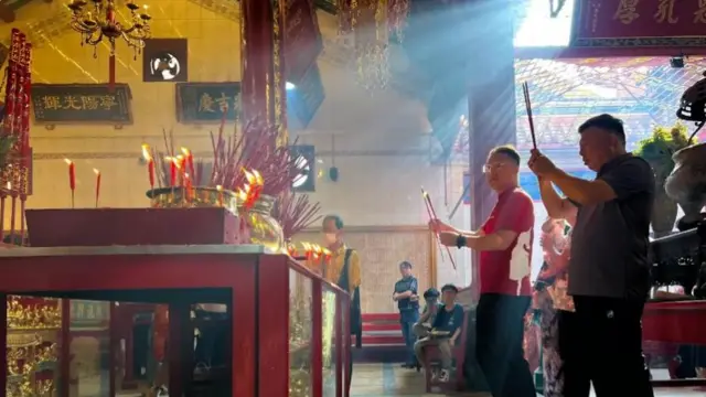 People praying in front of lit incense sticks at a temple