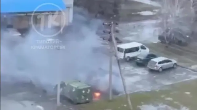Screengrab from a video showing thick smoke rising above a vehicle after struck by a drone and sparks visible around the blast site.