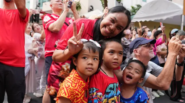 A woman flashes the peace sign while holding three children