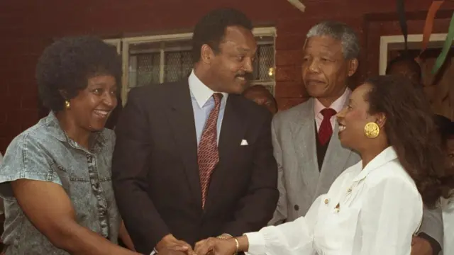 Jesse Jackson meeting with Nelson Mandela, accompanied by their wives who are smiling and shaking hands